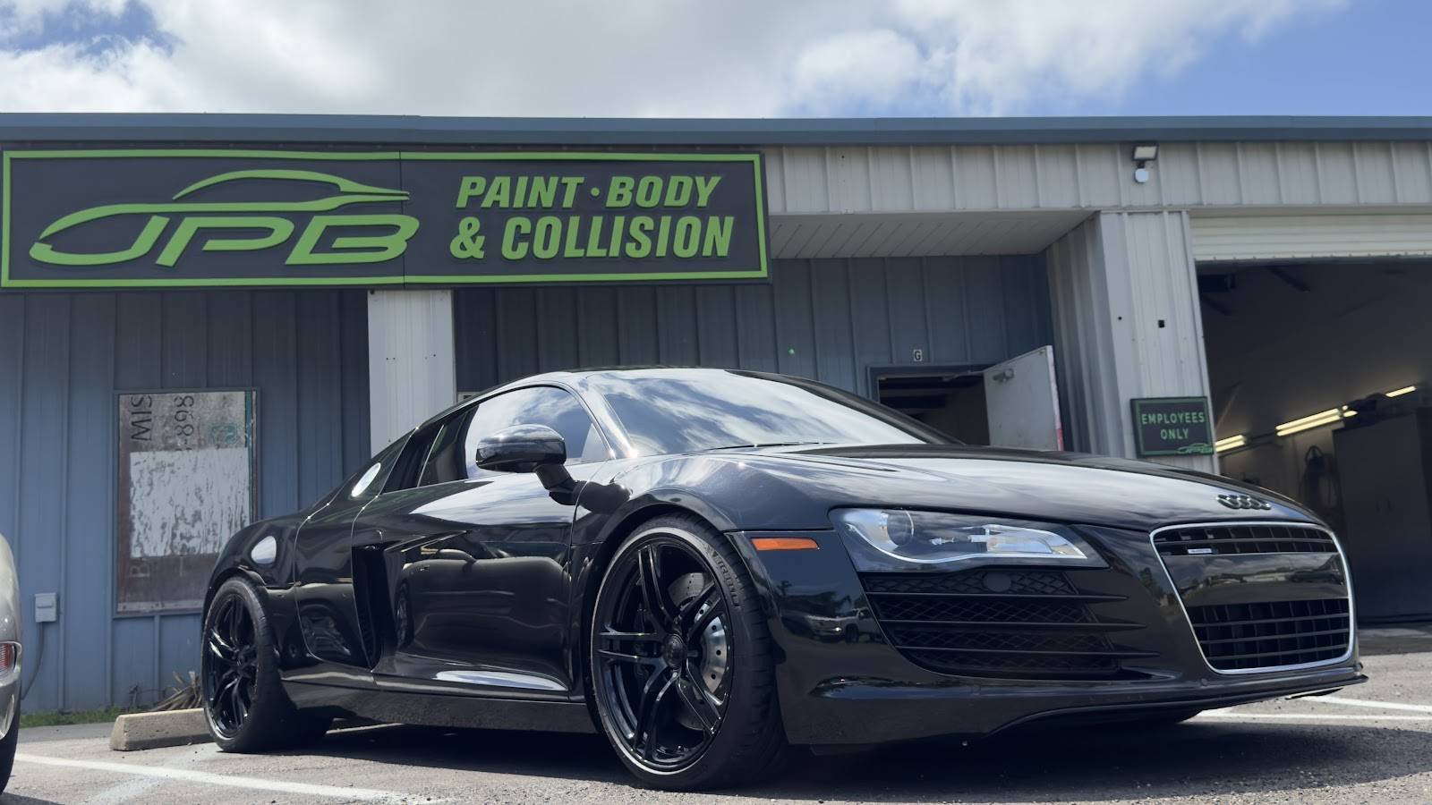 Glossy black Audi R8 parked under the green JPB Paint Body & Collision sign